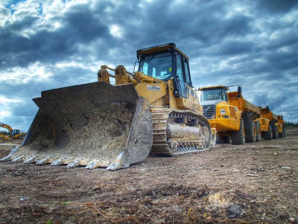 Mining equipment, dozer and three dump trucks lined up in a row.